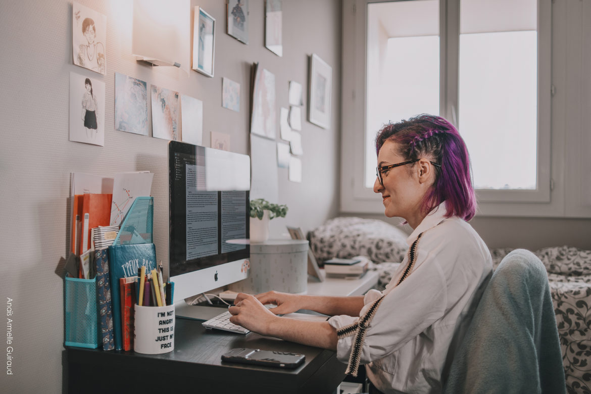 Photo illustrative montrant une femme aux cheveux violets écrivant à son bureau