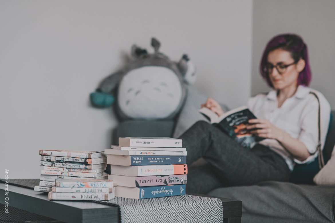 Femme lisant un livre avec une pile de livres sur la table
